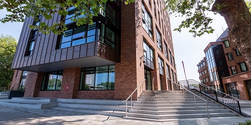 The exterior of a modern multi-storey building with a set of ten steps with handrails leading up to the entrance.